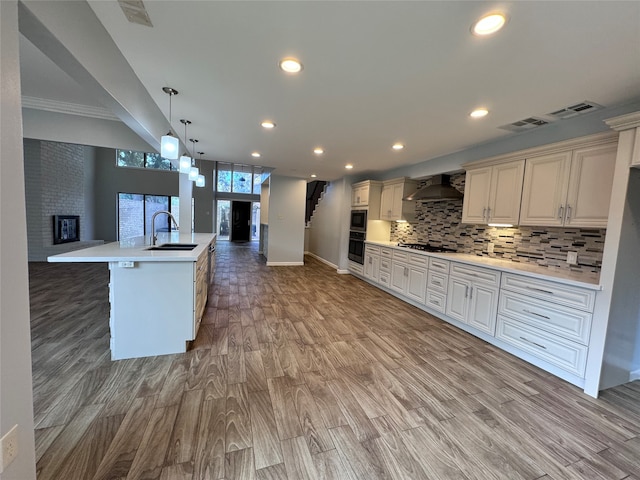 kitchen featuring a fireplace, light hardwood / wood-style floors, sink, wall chimney exhaust hood, and a large island