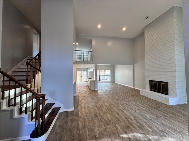 unfurnished living room featuring a fireplace, a towering ceiling, and wood-type flooring