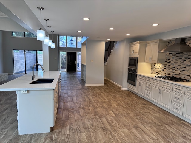 kitchen with hardwood / wood-style floors, a spacious island, stainless steel appliances, sink, and wall chimney range hood