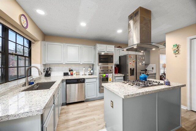 kitchen with island exhaust hood, appliances with stainless steel finishes, a center island, and sink