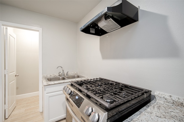 kitchen featuring gas stove, sink, ventilation hood, white cabinetry, and light hardwood / wood-style flooring