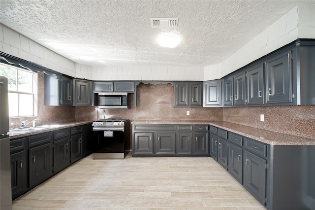 kitchen with a textured ceiling, light hardwood / wood-style floors, gray cabinets, and stainless steel appliances