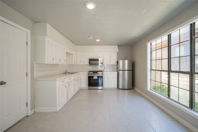 kitchen with appliances with stainless steel finishes, a textured ceiling, sink, and white cabinets