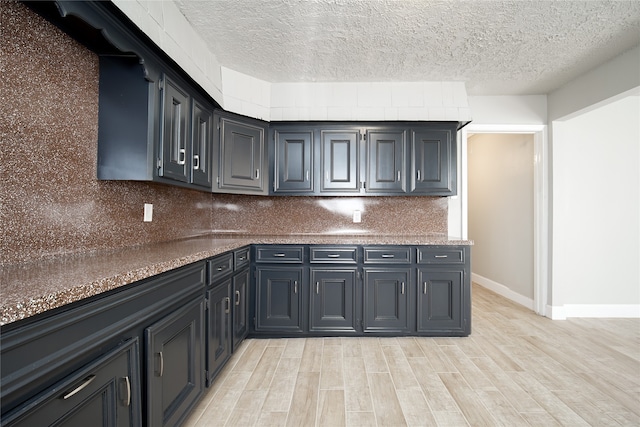 kitchen featuring light wood-type flooring, a textured ceiling, and dark stone countertops