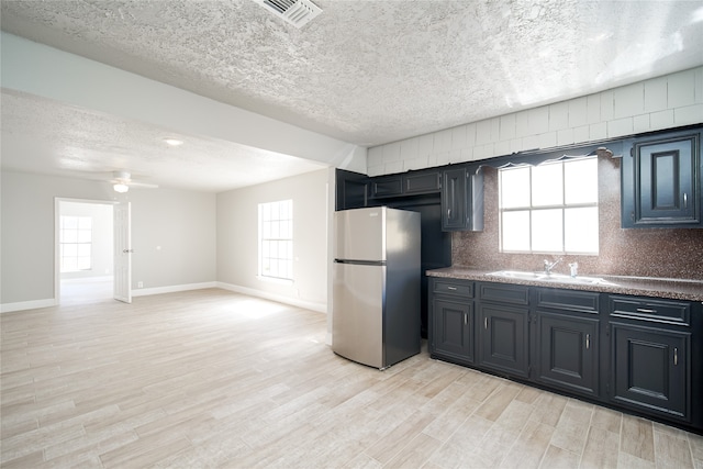 kitchen featuring light wood-type flooring, stainless steel refrigerator, a textured ceiling, and sink