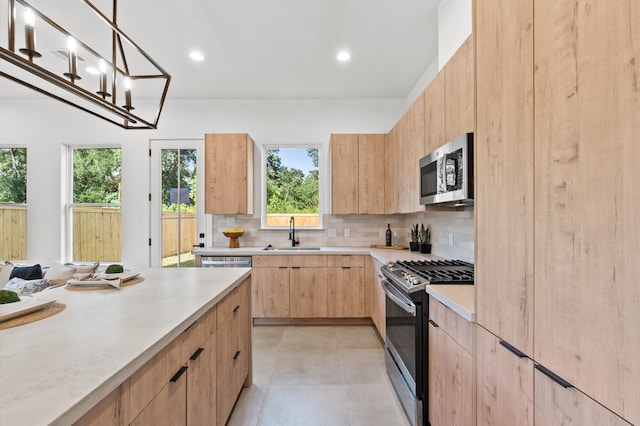 kitchen featuring backsplash, light brown cabinetry, stainless steel appliances, sink, and decorative light fixtures