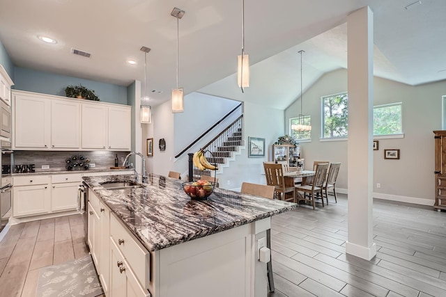 kitchen with sink, white cabinets, a kitchen island with sink, and hanging light fixtures