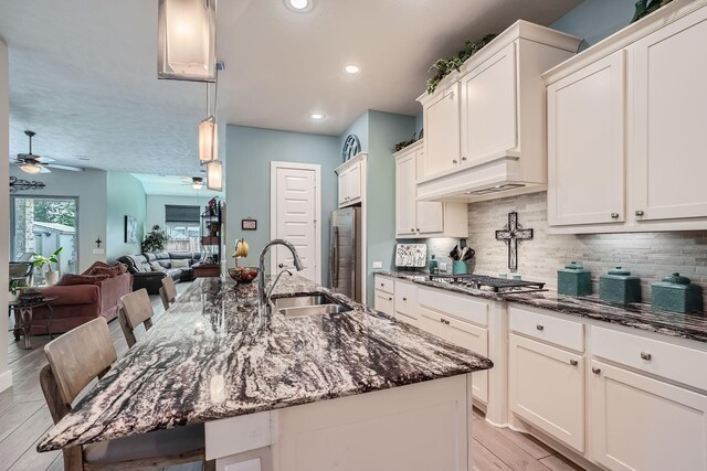 kitchen with ceiling fan, sink, dark stone countertops, stainless steel appliances, and a breakfast bar area