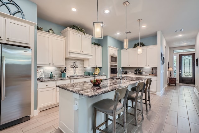 kitchen featuring an island with sink, dark stone counters, hanging light fixtures, and stainless steel appliances