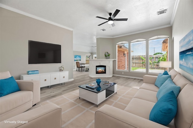 living room featuring ceiling fan, a fireplace, light wood-type flooring, and crown molding