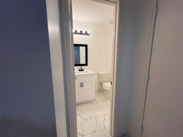 bathroom with a textured ceiling, vanity, and toilet