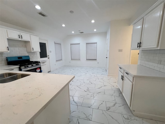 kitchen with decorative backsplash, stainless steel stove, light stone counters, and white cabinetry