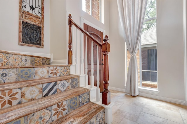 stairway with baseboards, stone tile flooring, and a towering ceiling