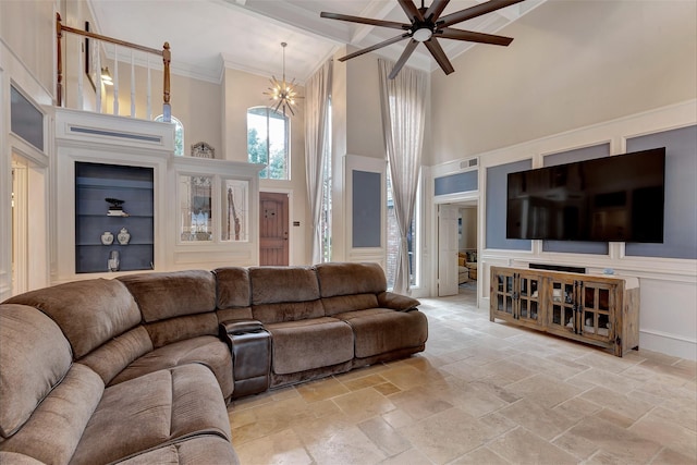 living room featuring a decorative wall, ceiling fan with notable chandelier, stone tile flooring, beamed ceiling, and a high ceiling