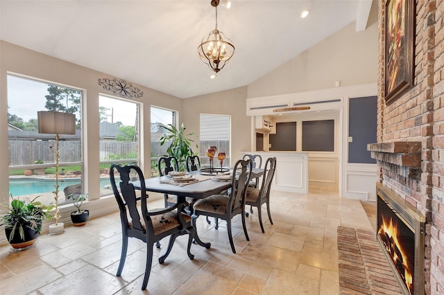 dining room with high vaulted ceiling, stone tile floors, a chandelier, a brick fireplace, and recessed lighting