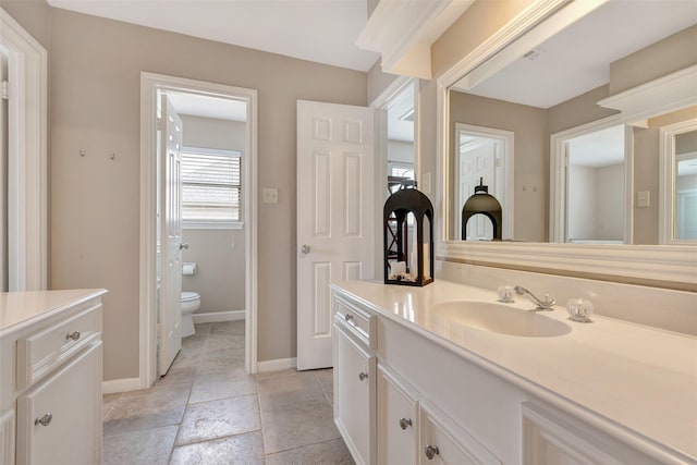 bathroom with toilet, stone tile flooring, vanity, and baseboards