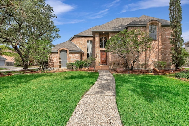 french country inspired facade featuring brick siding, a front yard, and roof with shingles