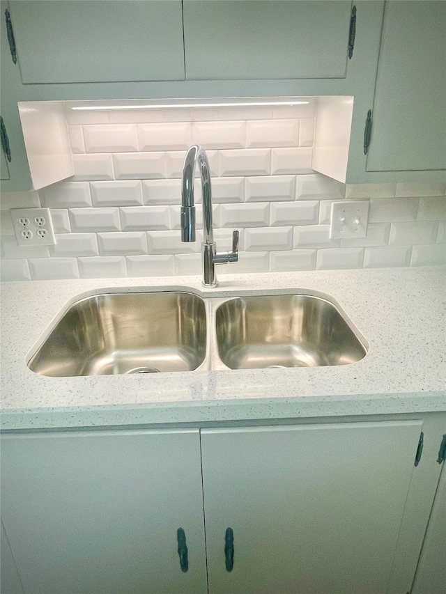 room details with light stone countertops, green cabinetry, decorative backsplash, and sink