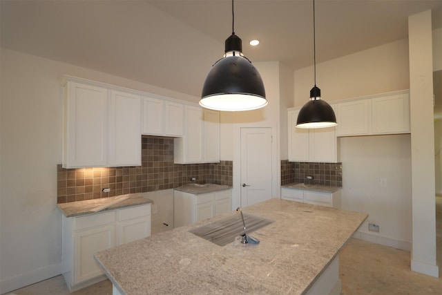 kitchen featuring pendant lighting, a center island with sink, white cabinets, and light stone counters