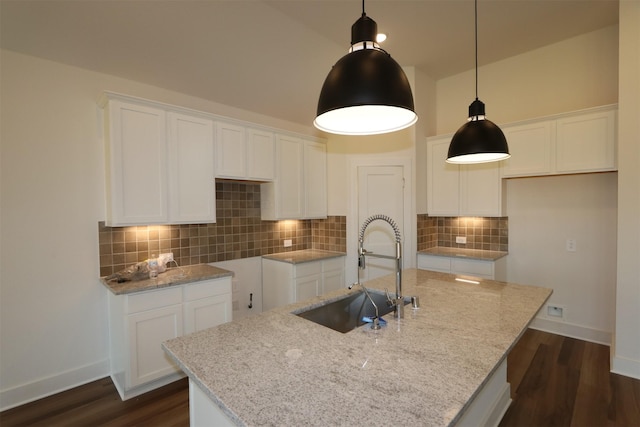 kitchen featuring dark wood-type flooring, white cabinets, an island with sink, and a sink