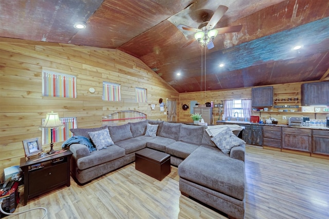 living area with light wood-type flooring, lofted ceiling, wooden walls, and ceiling fan