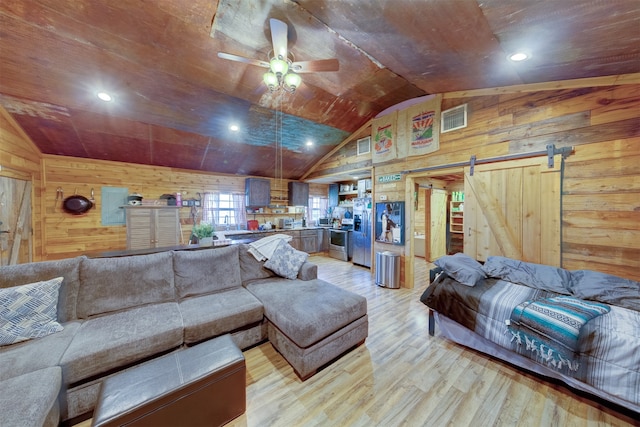 living room featuring vaulted ceiling, a barn door, wood walls, light wood-type flooring, and ceiling fan