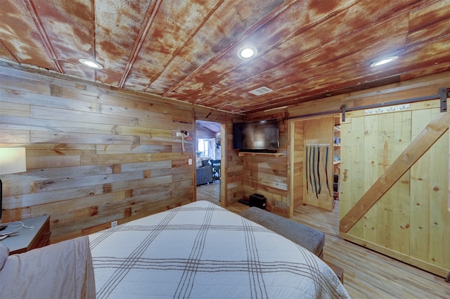 bedroom featuring wood-type flooring, wood walls, and a barn door