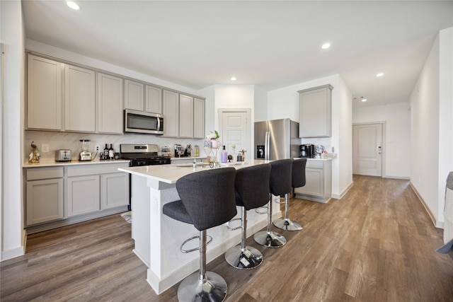 kitchen with light wood-type flooring, a kitchen bar, gray cabinetry, a center island with sink, and appliances with stainless steel finishes