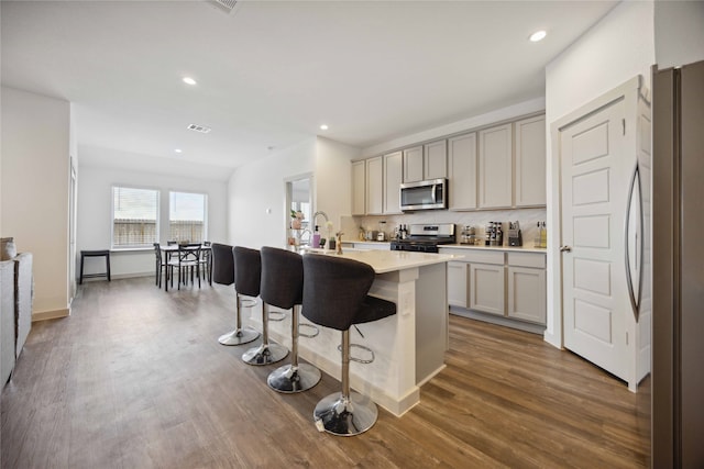 kitchen featuring a center island with sink, appliances with stainless steel finishes, dark hardwood / wood-style floors, and a breakfast bar