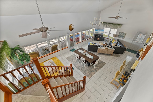 tiled living room featuring ceiling fan with notable chandelier and high vaulted ceiling