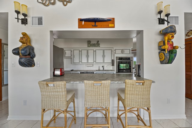 kitchen with sink, a breakfast bar area, oven, light tile patterned floors, and kitchen peninsula