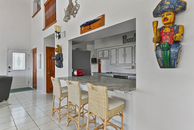 kitchen featuring light tile patterned floors, stainless steel refrigerator, a breakfast bar, gray cabinetry, and kitchen peninsula