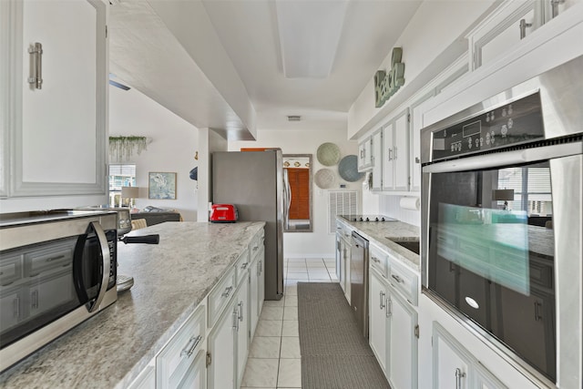 kitchen with stainless steel appliances, white cabinetry, light tile patterned floors, and light stone counters