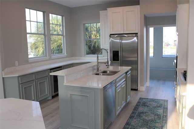 kitchen featuring appliances with stainless steel finishes, a kitchen island with sink, sink, and light hardwood / wood-style flooring