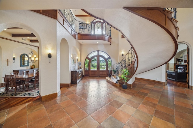 entryway featuring a high ceiling, arched walkways, a chandelier, french doors, and baseboards