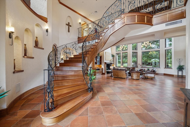 staircase with visible vents, baseboards, crown molding, and a high ceiling