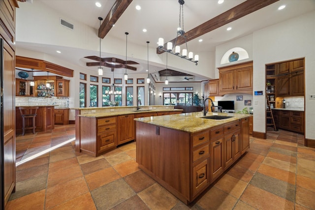 kitchen with tasteful backsplash, a large island with sink, beam ceiling, and stone tile floors