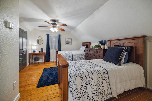 bedroom featuring light wood finished floors, a textured wall, lofted ceiling, and ceiling fan