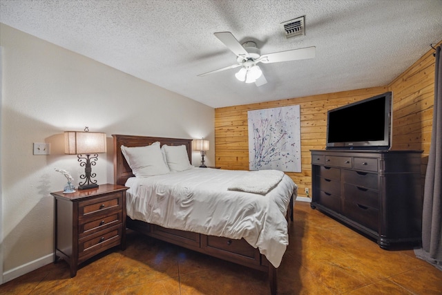bedroom with wooden walls, a textured ceiling, visible vents, and baseboards