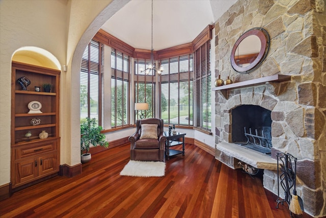 sitting room featuring a towering ceiling, a fireplace, wood finished floors, baseboards, and an inviting chandelier
