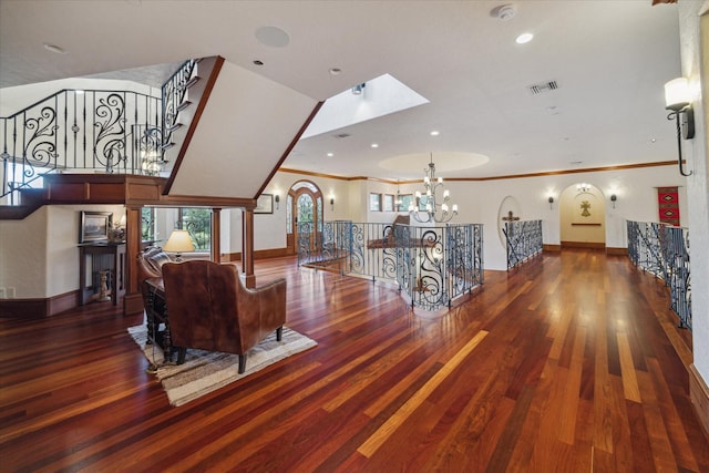 living area with visible vents, wood finished floors, baseboards, an inviting chandelier, and ornamental molding