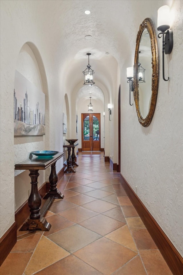 hall featuring arched walkways, a textured wall, french doors, and lofted ceiling