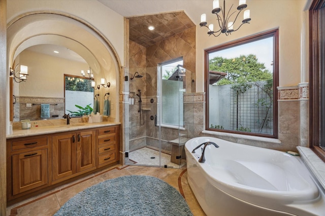 full bathroom with a garden tub, tile walls, a stall shower, vanity, and a notable chandelier