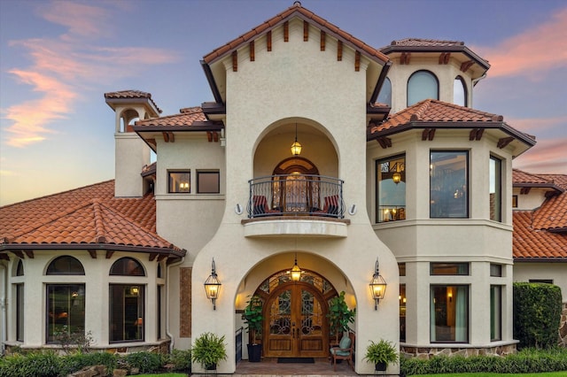 back of property at dusk featuring french doors, stucco siding, a tile roof, and a balcony