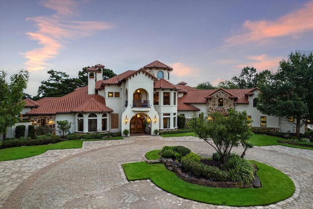 mediterranean / spanish home with a balcony, curved driveway, stucco siding, a chimney, and a tiled roof
