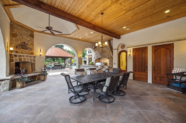 view of patio with a ceiling fan, outdoor dining area, exterior kitchen, an outdoor stone fireplace, and a gazebo