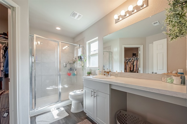 bathroom featuring wood-type flooring, vanity, toilet, and a shower with shower door