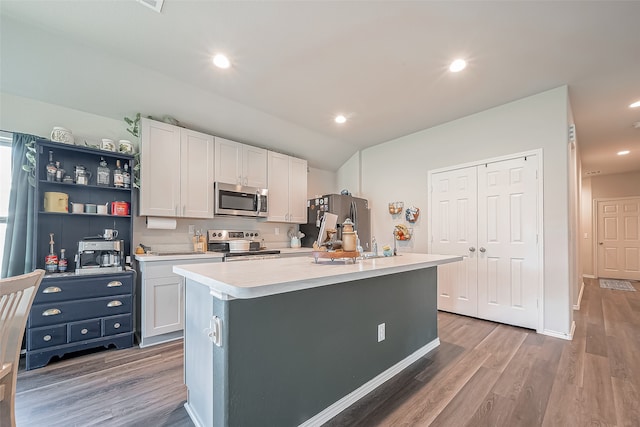 kitchen with wood-type flooring, white cabinetry, appliances with stainless steel finishes, and a kitchen island with sink