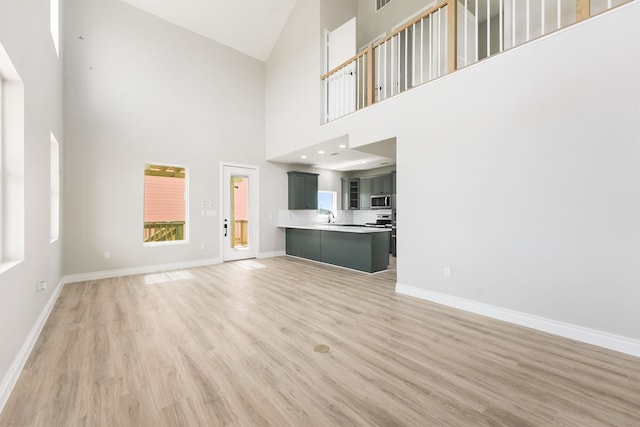 unfurnished living room with high vaulted ceiling, hardwood / wood-style floors, and sink