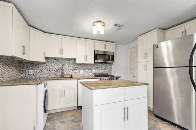 kitchen with appliances with stainless steel finishes, white cabinetry, a kitchen island, a textured ceiling, and washer / dryer